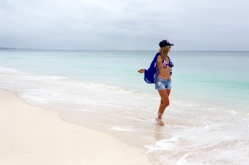 Woman holidaying on a beach in Australia. She has a flag draped over her shoulder