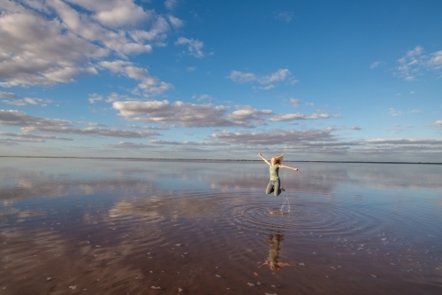 Woman jumping in the air over a salt lake. - Australian Stock Image