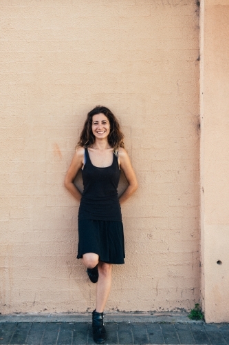 woman leaning against brick wall, smiling - Australian Stock Image