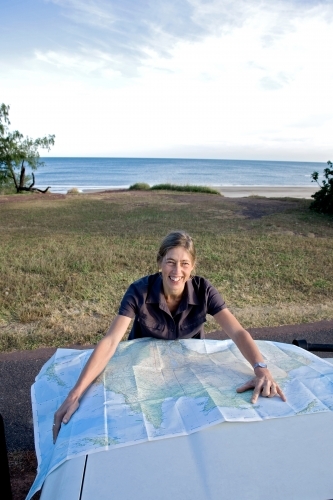 Woman leaning on bonnet of car with map, smiling at the camera - Australian Stock Image