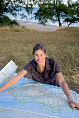 Woman leaning on bonnet of car with map, smiling at the camera - Australian Stock Image