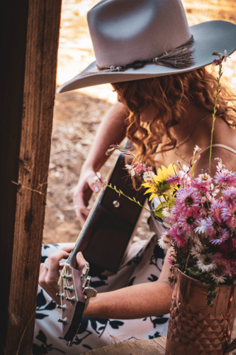 Woman playing a guitar with flowers in country setting - Australian Stock Image