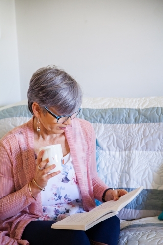 Woman reading a book on the lounge with cup of tea - Australian Stock Image