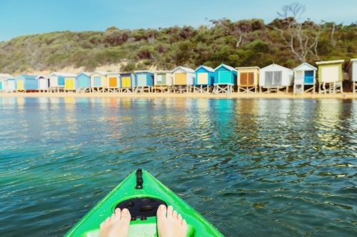 woman's feet in kayak in the ocean with colorful beach huts on the shore - Australian Stock Image