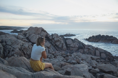 Woman sitting on rocky coastline of South West WA looking out over ocean - Australian Stock Image