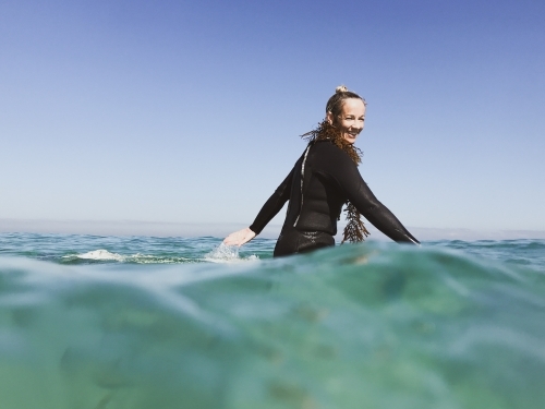 Woman sitting on surfboard paddling arms wearing seaweed - Australian Stock Image
