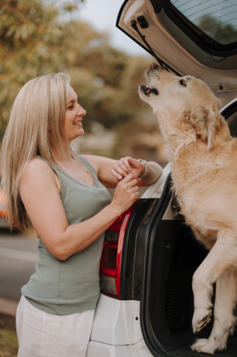 Woman standing beside the car with her dog in the car boot. - Australian Stock Image