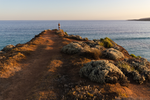 Woman standing on desert headland with vast view of the ocean at sunset in South Australia - Australian Stock Image