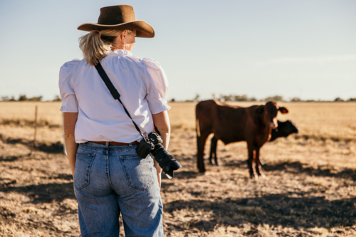 Woman standing with DSLR camera standing in a dry grassy farm paddock - Australian Stock Image