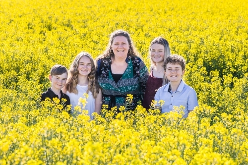 Woman standing with four children family in canola paddock on farm