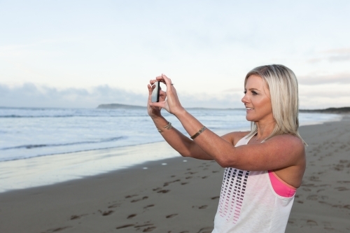 woman taking a photo at the beach on her phone