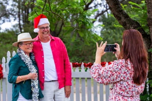 Woman taking photos with phone of happy senior couple - Australian Stock Image