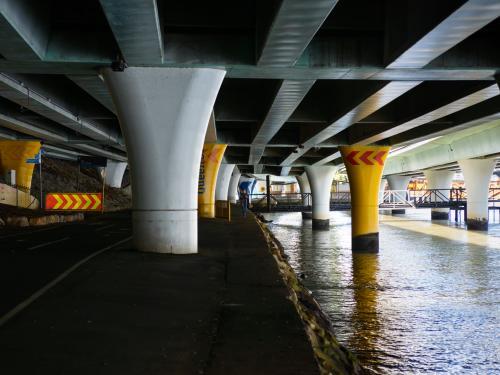 Woman walking on the banks of a river under an expressway - Australian Stock Image