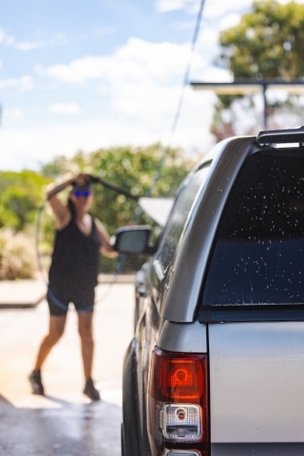 Woman washing vehicle in self-service car wash bay - Australian Stock Image