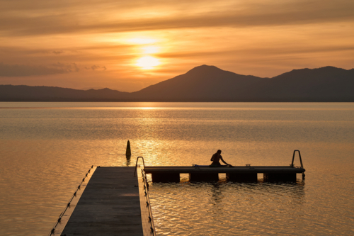 woman watching sunset while sitting on jetty - Australian Stock Image