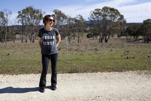 Woman wearing vegan slogan t-shirt standing on rural dirt road - Australian Stock Image