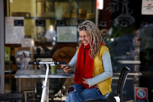 Woman with dreadlocks at cafe with electric scooter - Australian Stock Image