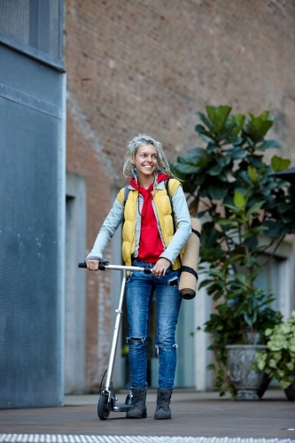 Woman with dreadlocks on electric scooter going to city yoga class - Australian Stock Image