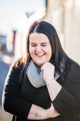 Woman with long hair wearing scarf laughing with eyes closed - Australian Stock Image