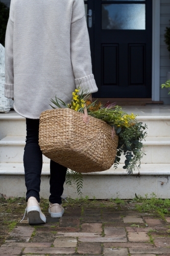 Woman with market basket of wild flowers walking along footpath - Australian Stock Image