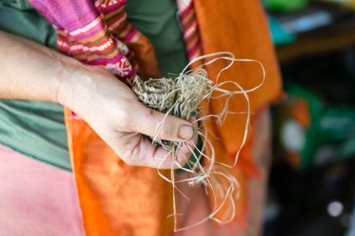 Woman with orange scarf holding a roll of fibers for weaving. - Australian Stock Image