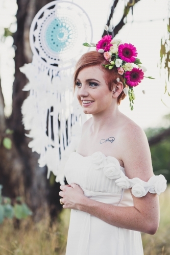 Woman with tattoo wearing flowers in hair standing with dreamcatcher - Australian Stock Image