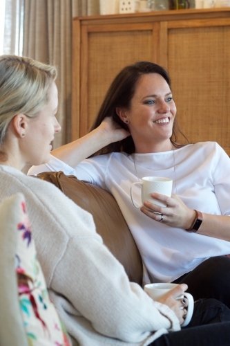 Women chatting on lounge with hot drinks - Australian Stock Image