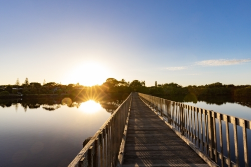 Wooden footbridge leading across Simpsons Creek at Brunswick Heads at sunrise - Australian Stock Image