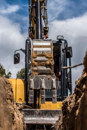 Yellow excavator digging trench against cloudy sky - Australian Stock Image