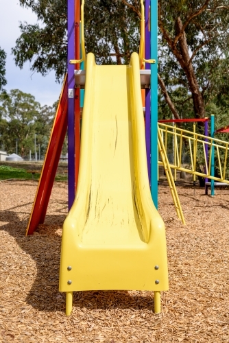 Yellow slide in colourful childrens playground - Australian Stock Image