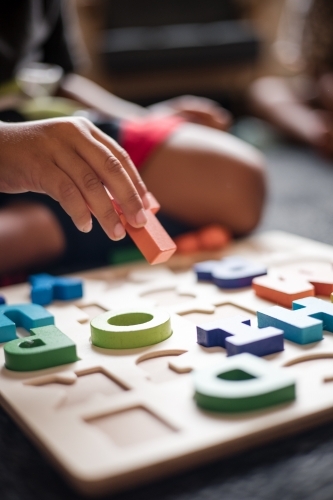 Young Aboriginal boy playing with alphabet letter puzzle pieces - Australian Stock Image