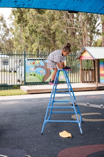 Young Aboriginal girl climbing over a ladder at preschool - Australian Stock Image