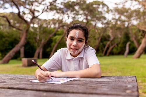 Young Aboriginal girl sitting and drawing at an outdoor table - Australian Stock Image