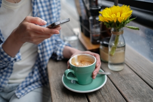 Young adult using mobile and holding cup of coffee - Australian Stock Image