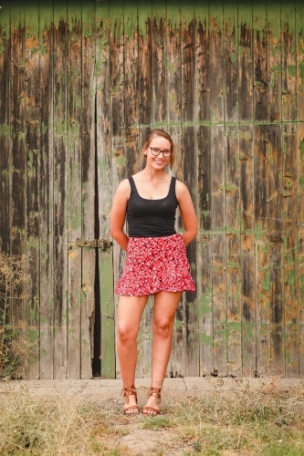 Young adult woman standing in front of rustic barn door with chipped paint - Australian Stock Image