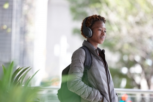 Young African woman listening to music wearing wireless headphones in city - Australian Stock Image