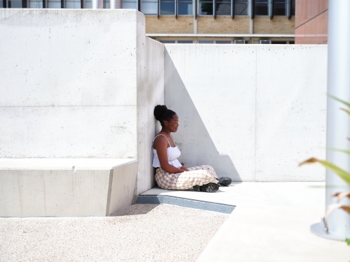 Young African woman sitting against a concrete wall - Australian Stock Image