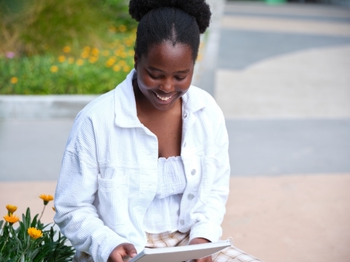 Young African woman sitting in university courtyard with notebook - Australian Stock Image