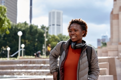 Young African woman wearing wireless headphones in city - Australian Stock Image