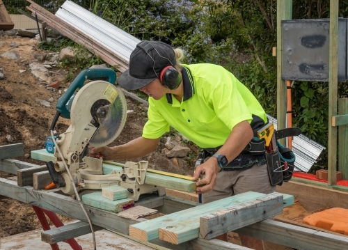 Young apprentice builder cutting timber with drop saw on residential construction site - Australian Stock Image