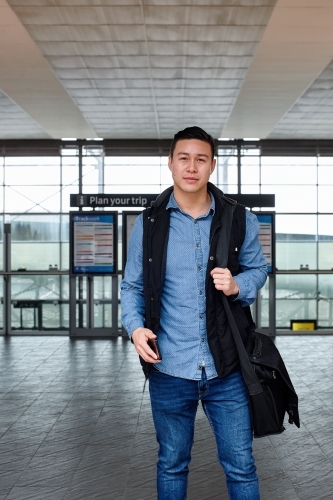 Young Asian commuter holding mobile phone waiting at train station entrance - Australian Stock Image