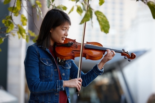 Young Asian female violin player practising outdoors - Australian Stock Image