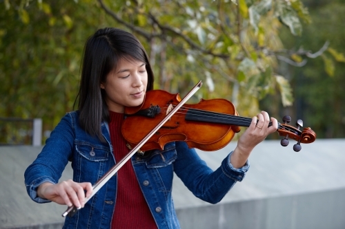 Young Asian female violin player practising outdoors - Australian Stock Image