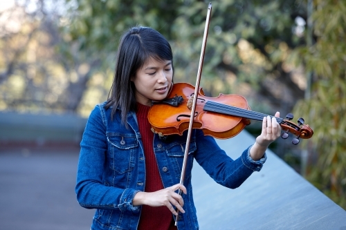 Young Asian female violin player practising outdoors - Australian Stock Image