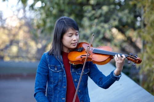 Young Asian female violin player practising outdoors - Australian Stock Image