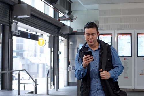 Young Asian man checking mobile device at train station - Australian Stock Image