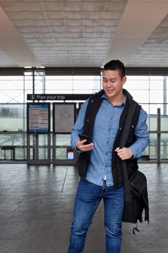 Young Asian man checking mobile device at train station - Australian Stock Image