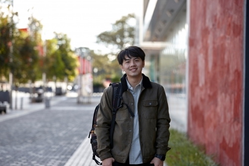 Young Asian student standing outside the university campus - Australian Stock Image