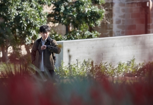 Young Asian university student standing on-campus checking smart watch - Australian Stock Image