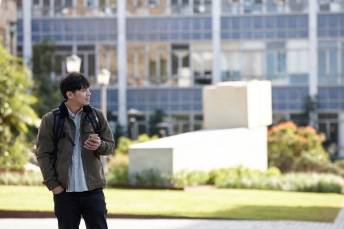 Young Asian university student using mobile phone on-campus - Australian Stock Image